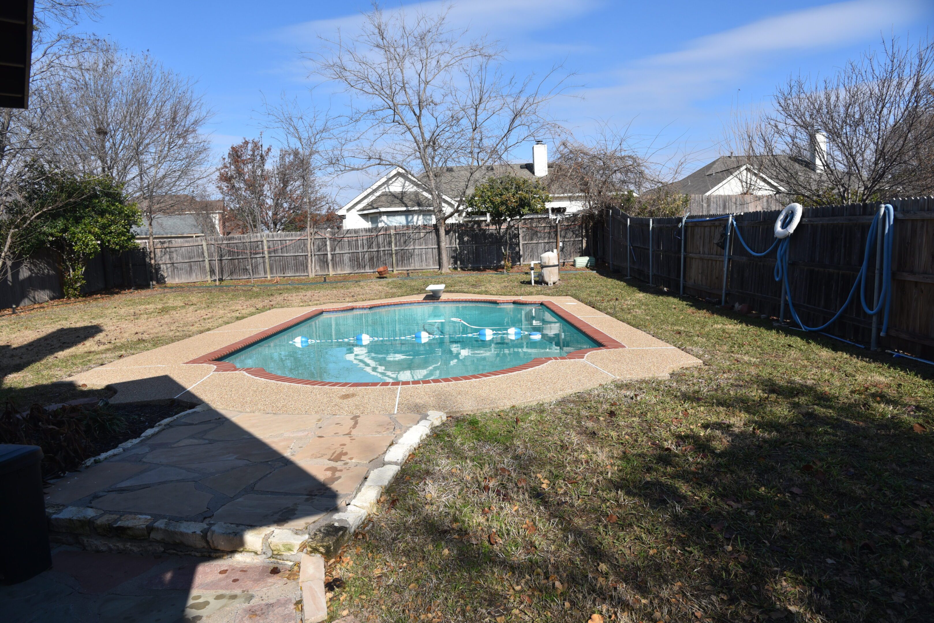 Backyard pool with surrounding fence and trees.