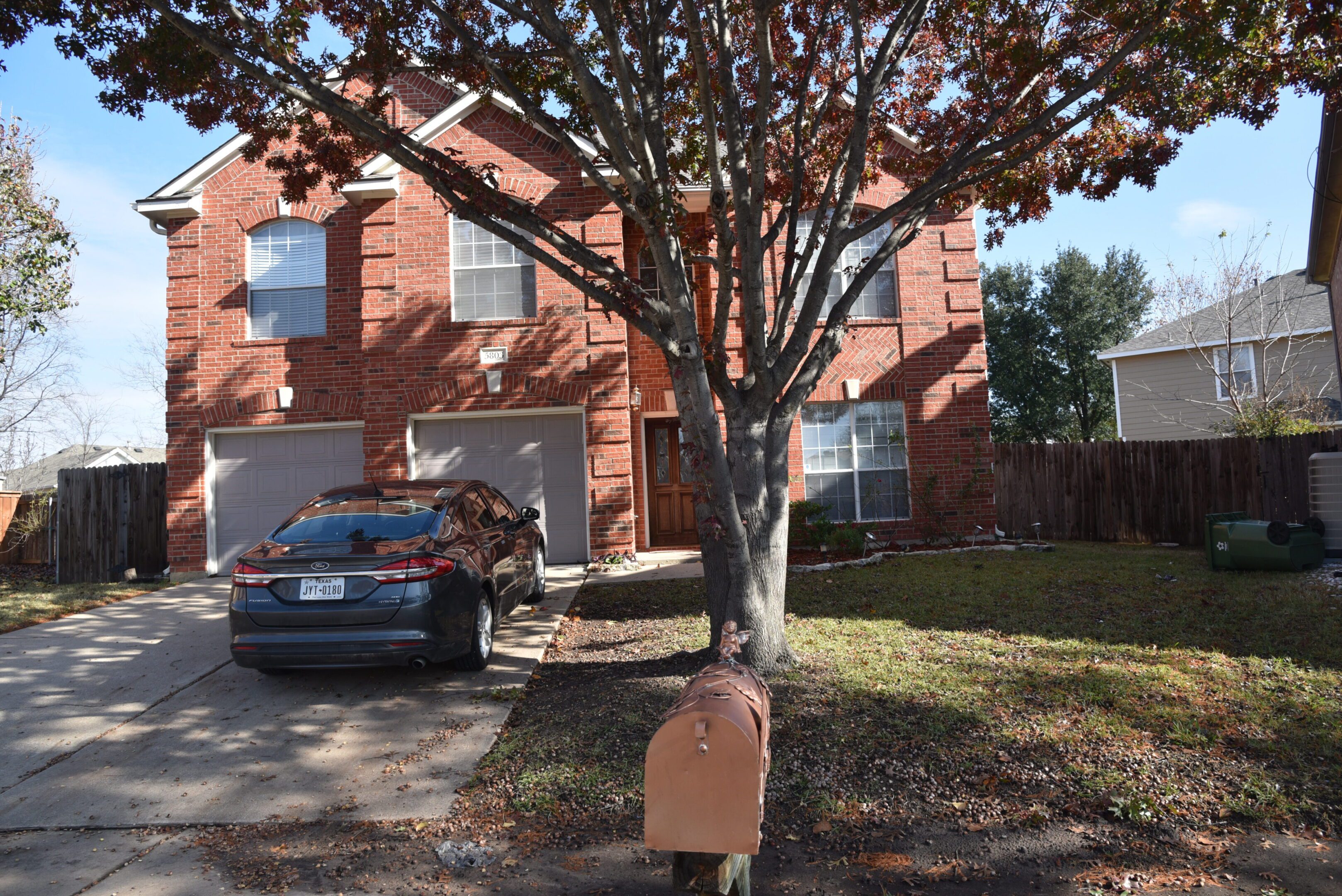 Brick house with car and tree outside.