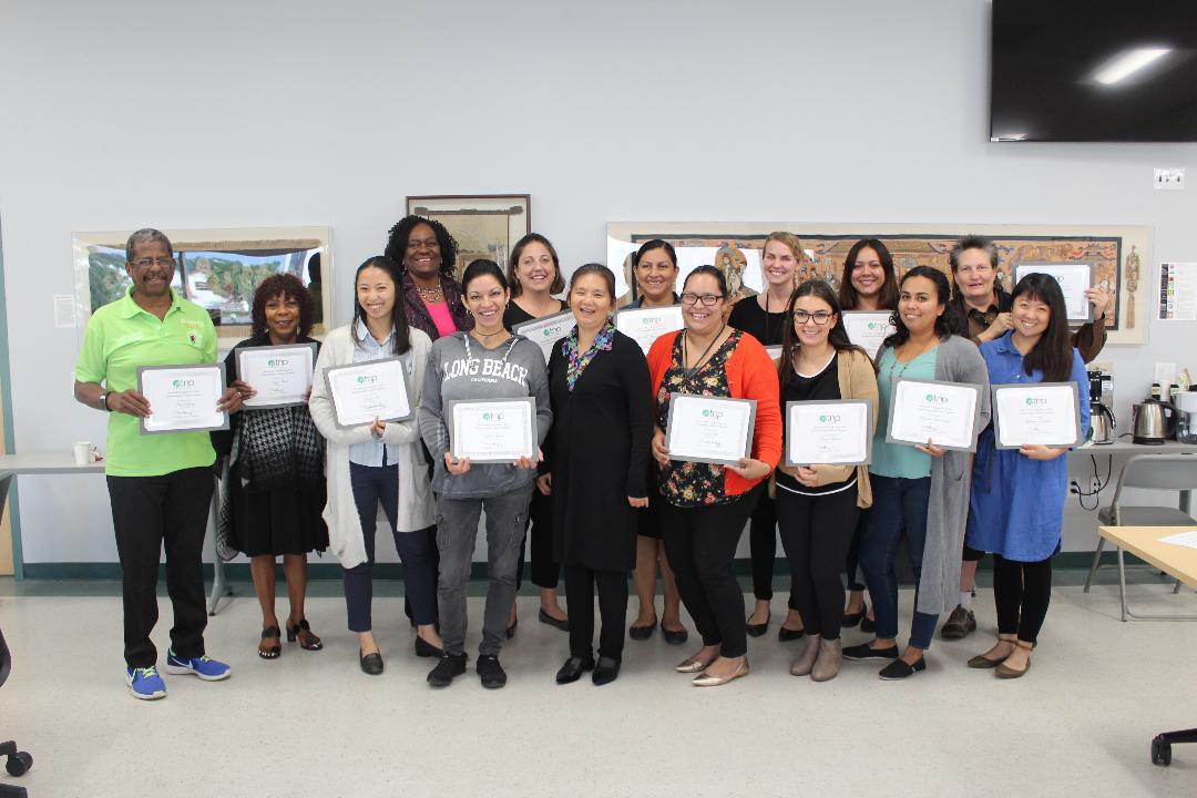 Group holding certificates, smiling in classroom setting.