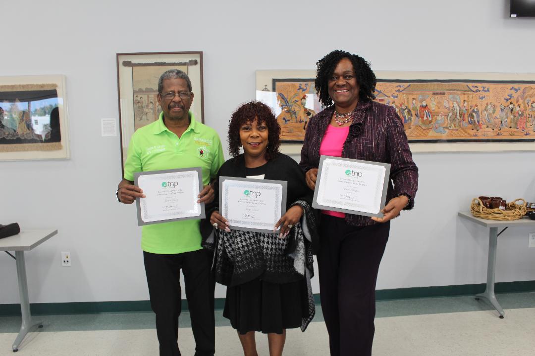 Three people proudly holding certificates indoors.