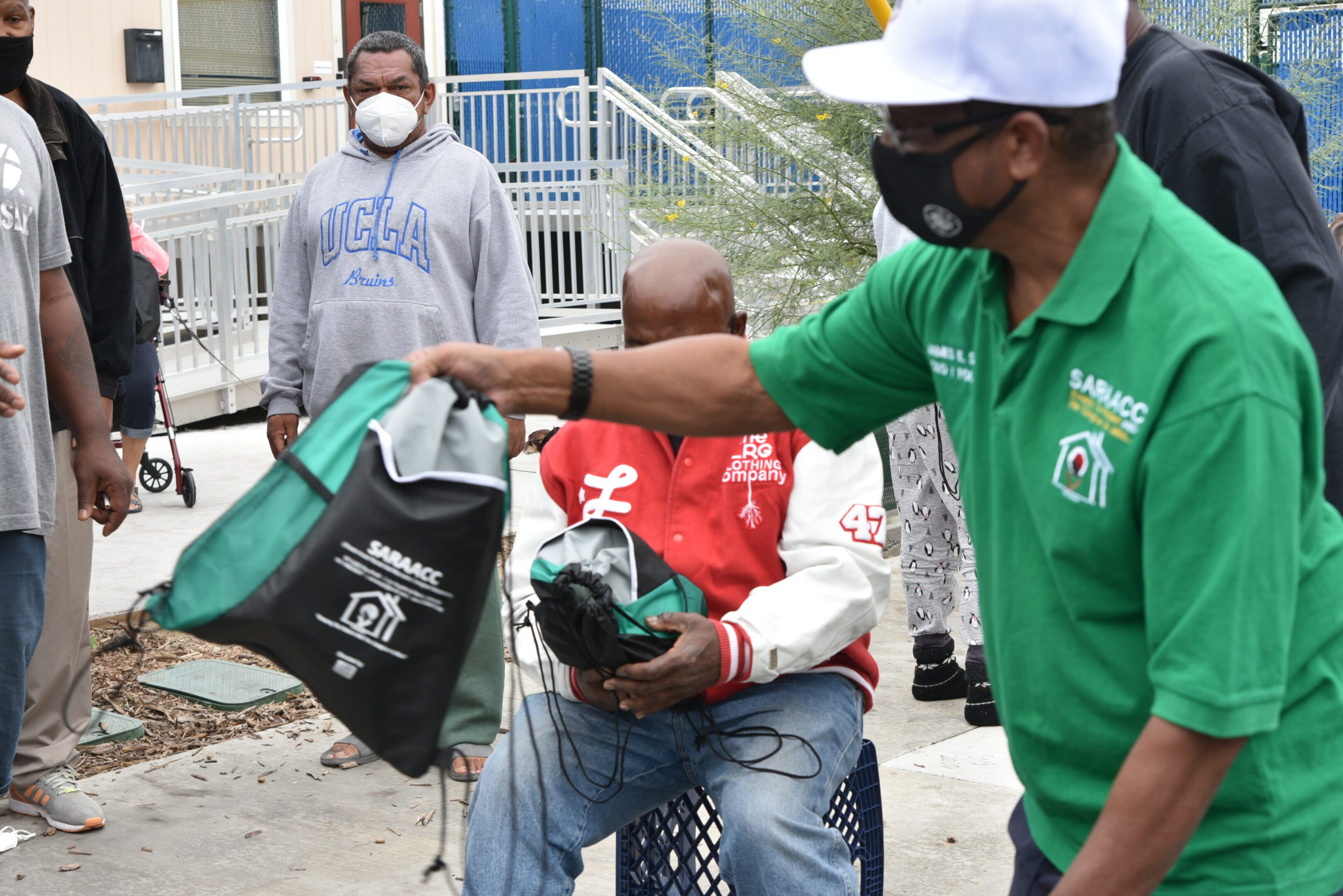 Man distributing bags to seated person outdoors.
