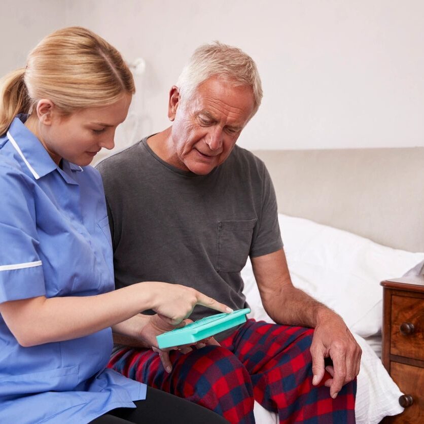 Caregiver assisting elderly man with medication.