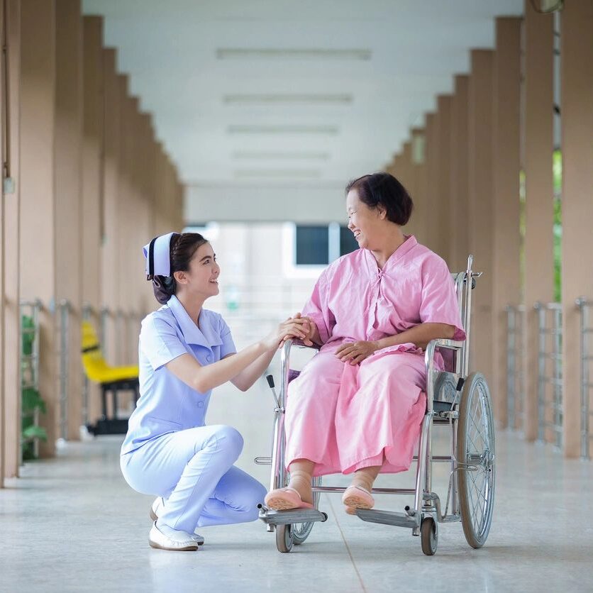 Nurse assisting woman in wheelchair, smiling.